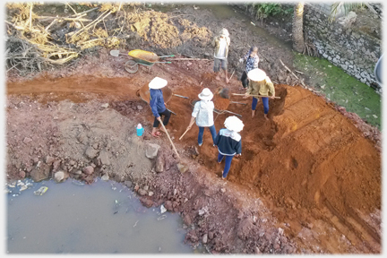 A group of six women spreading soil that has been dumped to cover the area.