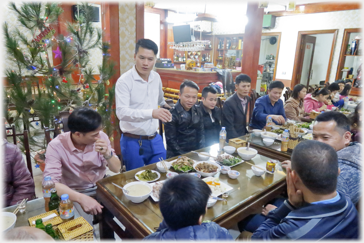 Han standing at a long table raising a glass.