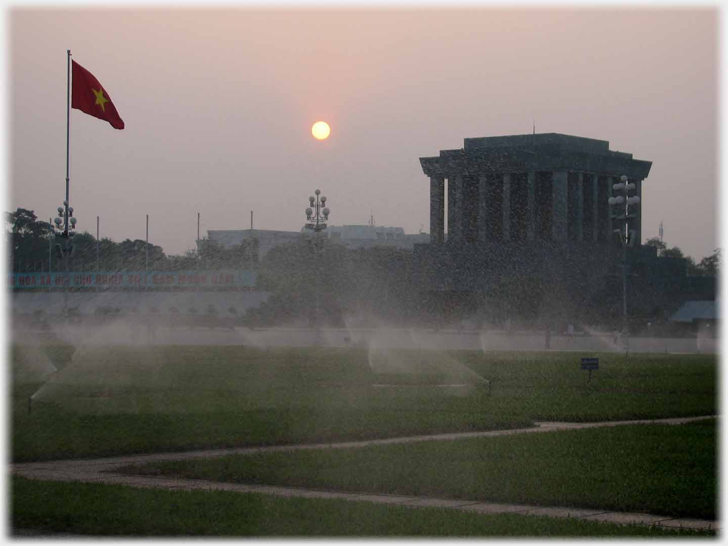 Setting sun between flag and mausoleum, air filled with spray.