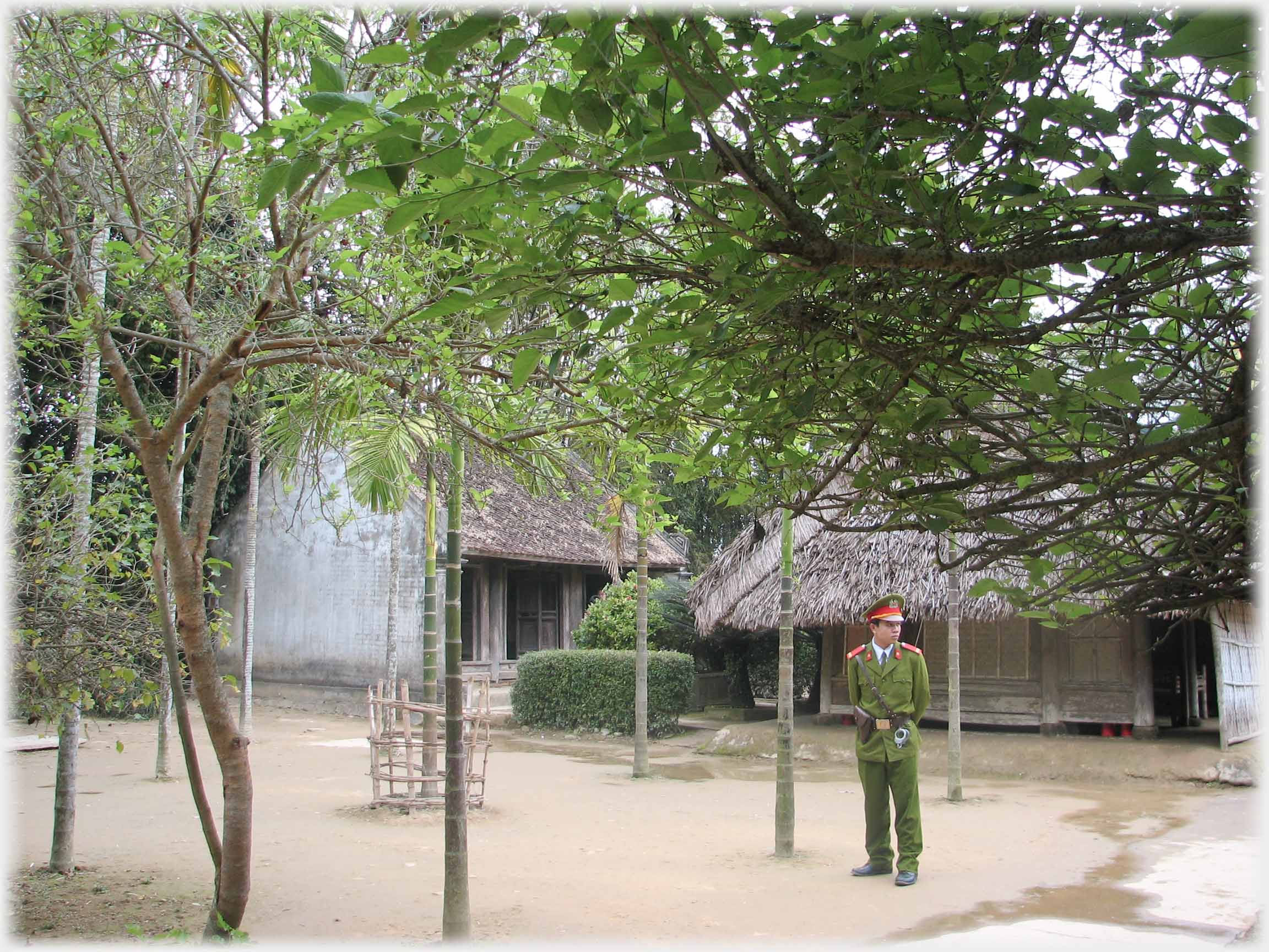 Soldier standing in courtyard area of thatched houses.
