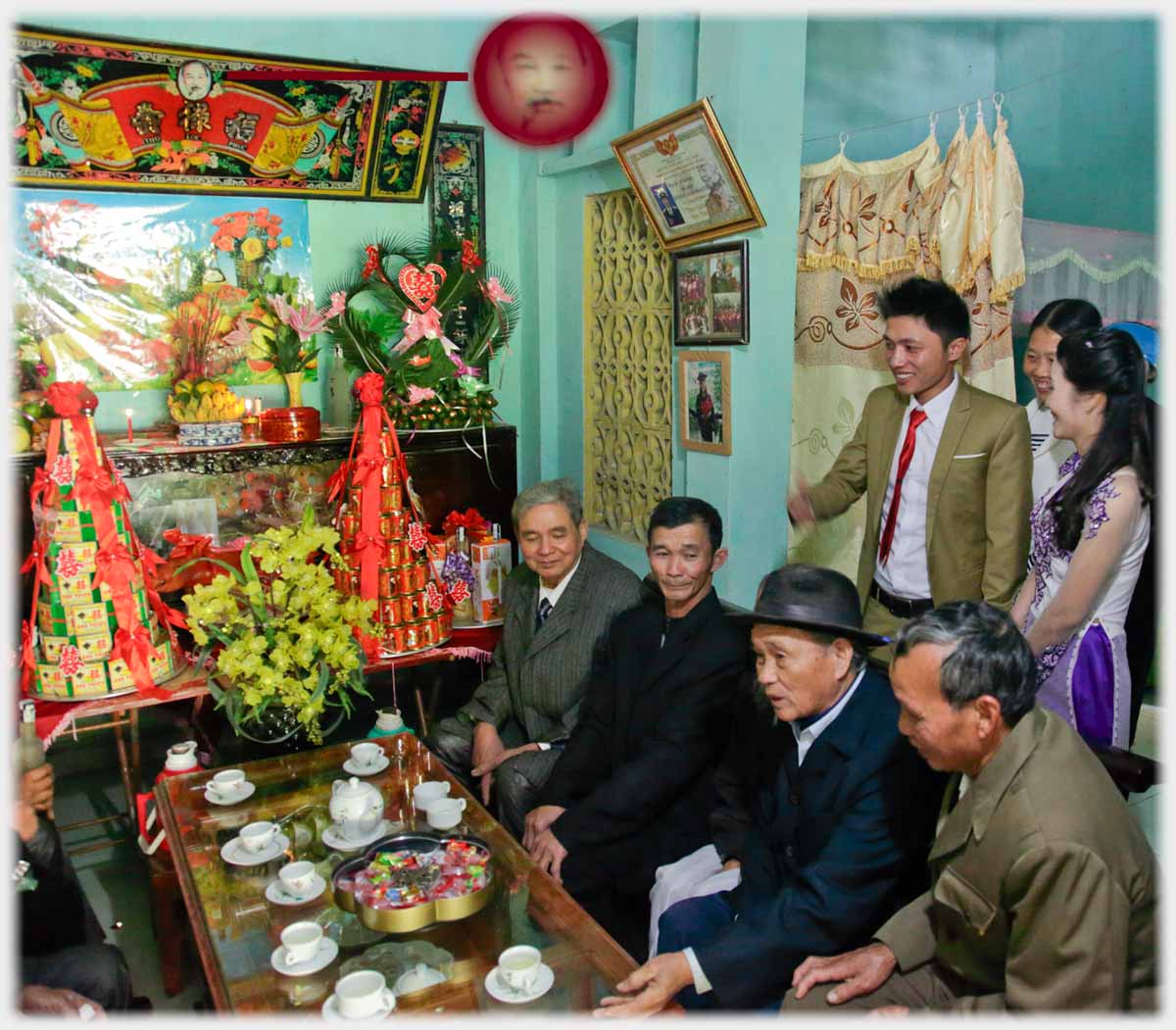 House reception room with bride and groom behind seated family, small face of Uncle Ho indicated.