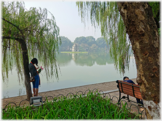 Woman texting, man dozing by Lake.