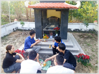 Group sitting at meal beside a grave monument.