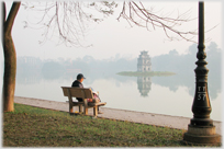 Figure sitting by misty lake.