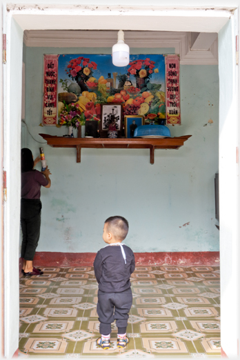 Infant back to camera standing, shelf altar above.