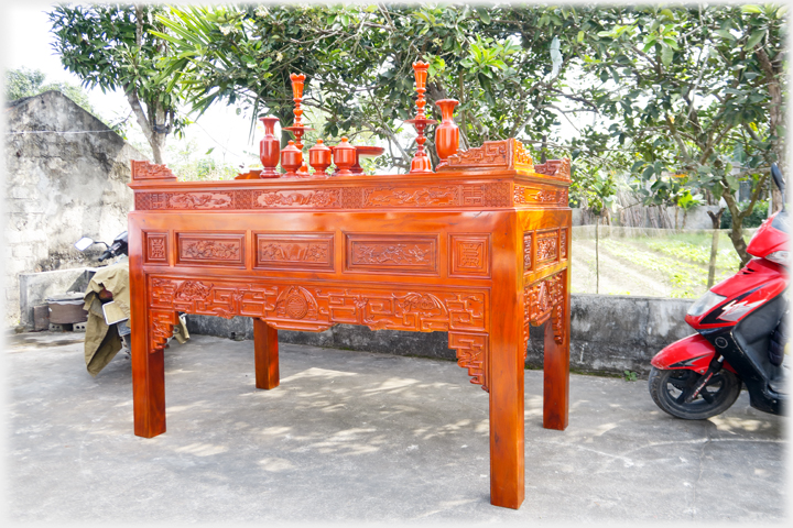 A large pristine altar sitting in the garden next to a motorbike.