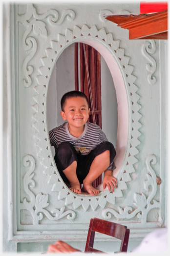 Child squatting in, and framed by, an oval window within the house.