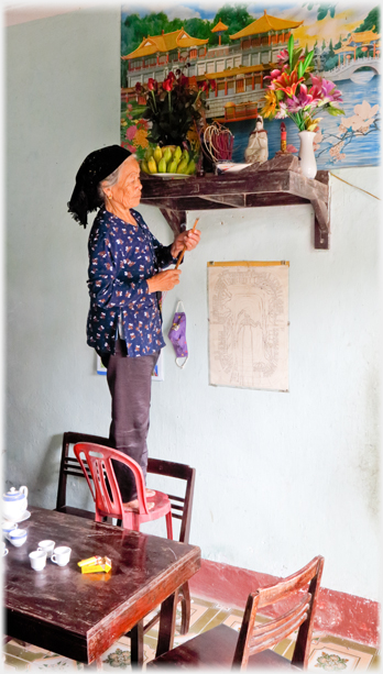 Han's mother standing on a chair preparing insence for her family's altar.