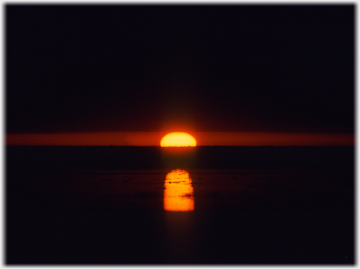 Sun half below horizon with reflection in mud.