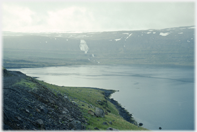 Fjord with distant waterfall and snow patches.