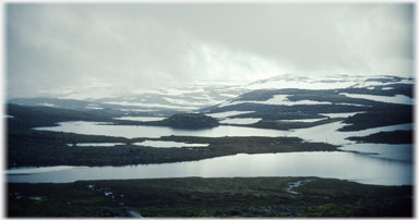 Water and snow in folds of landscape under low cloud.