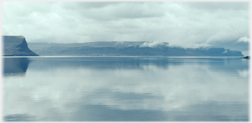 Calm sea stretching away to high cliffs and cloud.