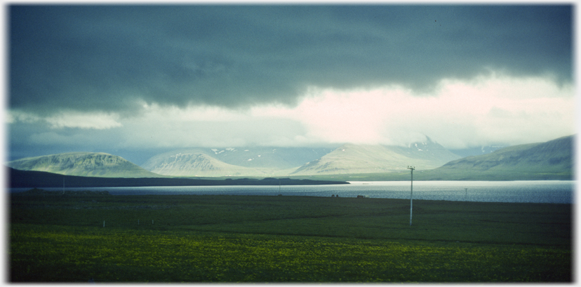 Lourering black clouds with sunlight coming through to a fjord.