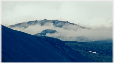 Cloud gathered aroound a black hillside.