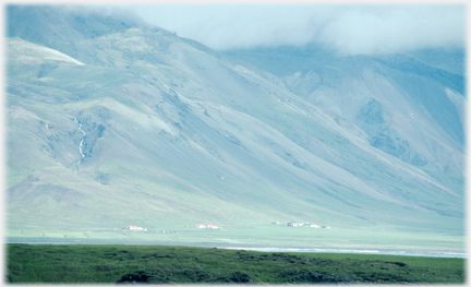 Steep slopes rising into the clouds with a few houses below.