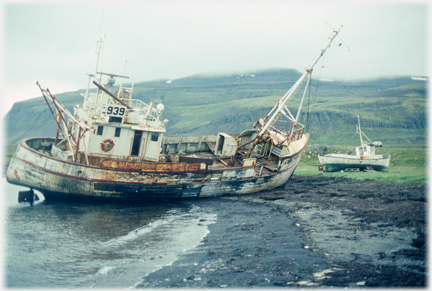 Fishing boat at steep angle on shore, sides
		rotting.