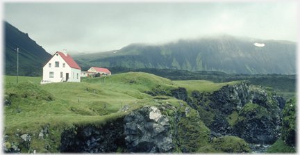 Modern houses on undulating grassland with
		mountains beyond.