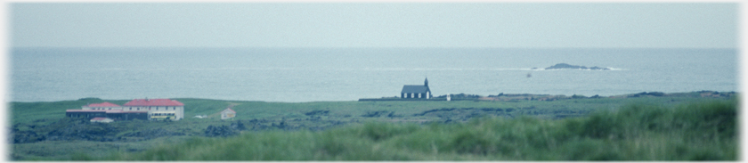 Church near shore with sea beyond and a small number
		of houses.