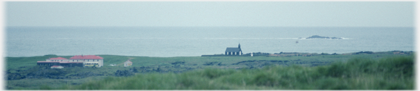 Church near shore with sea beyond and a small number
		of houses.