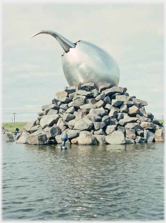 Metal sculpture of egg with pointed
		curved beak protruding.