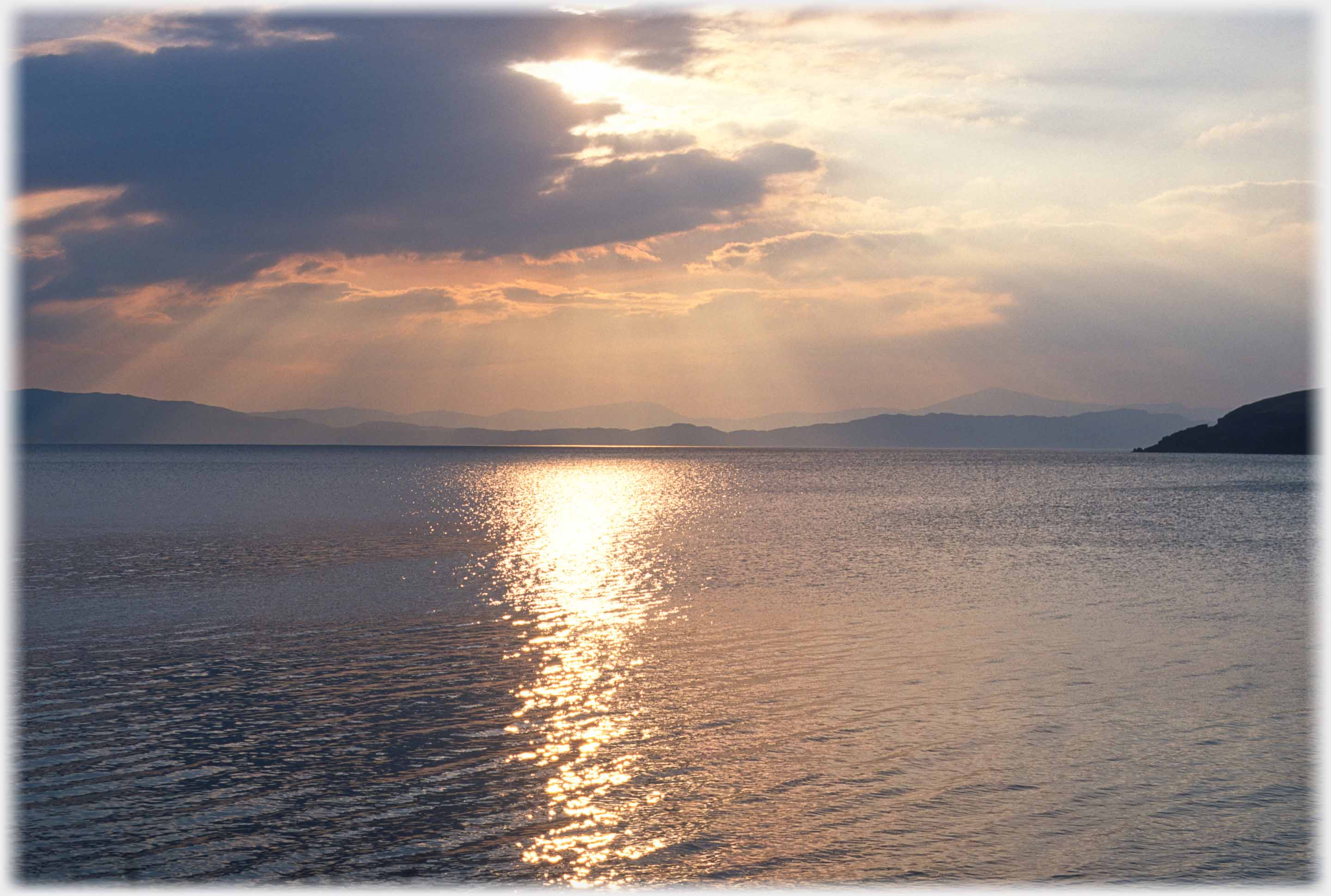 Shafts of sunlight and reflections on the sea with land on the horizon.