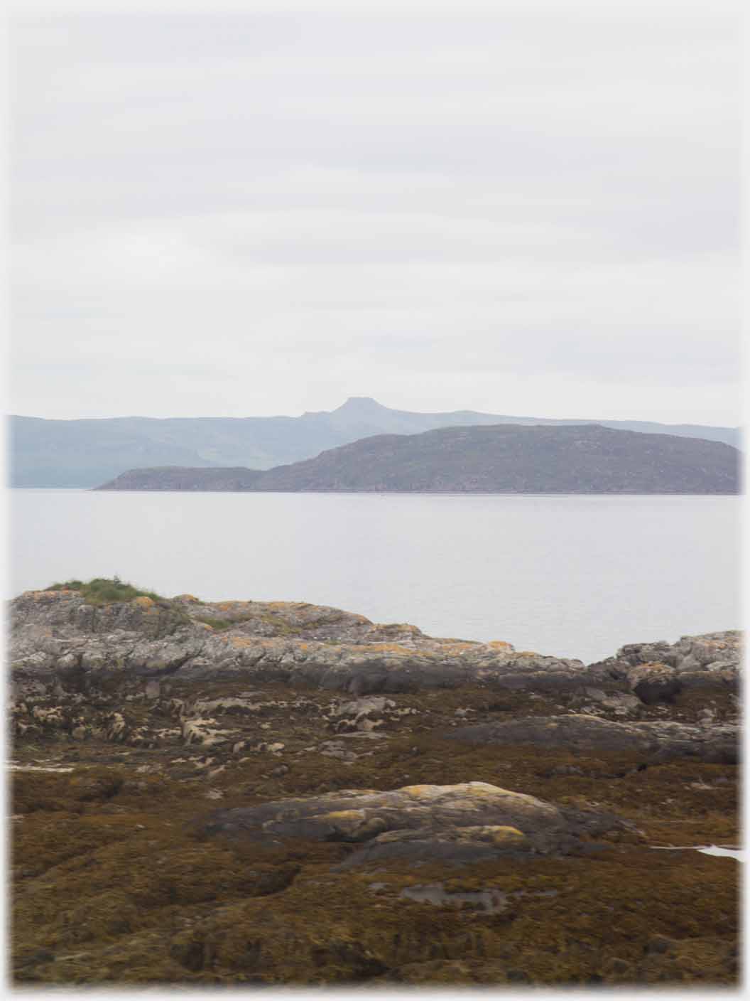 Sea with land beyond and the outline of a cut off hill.