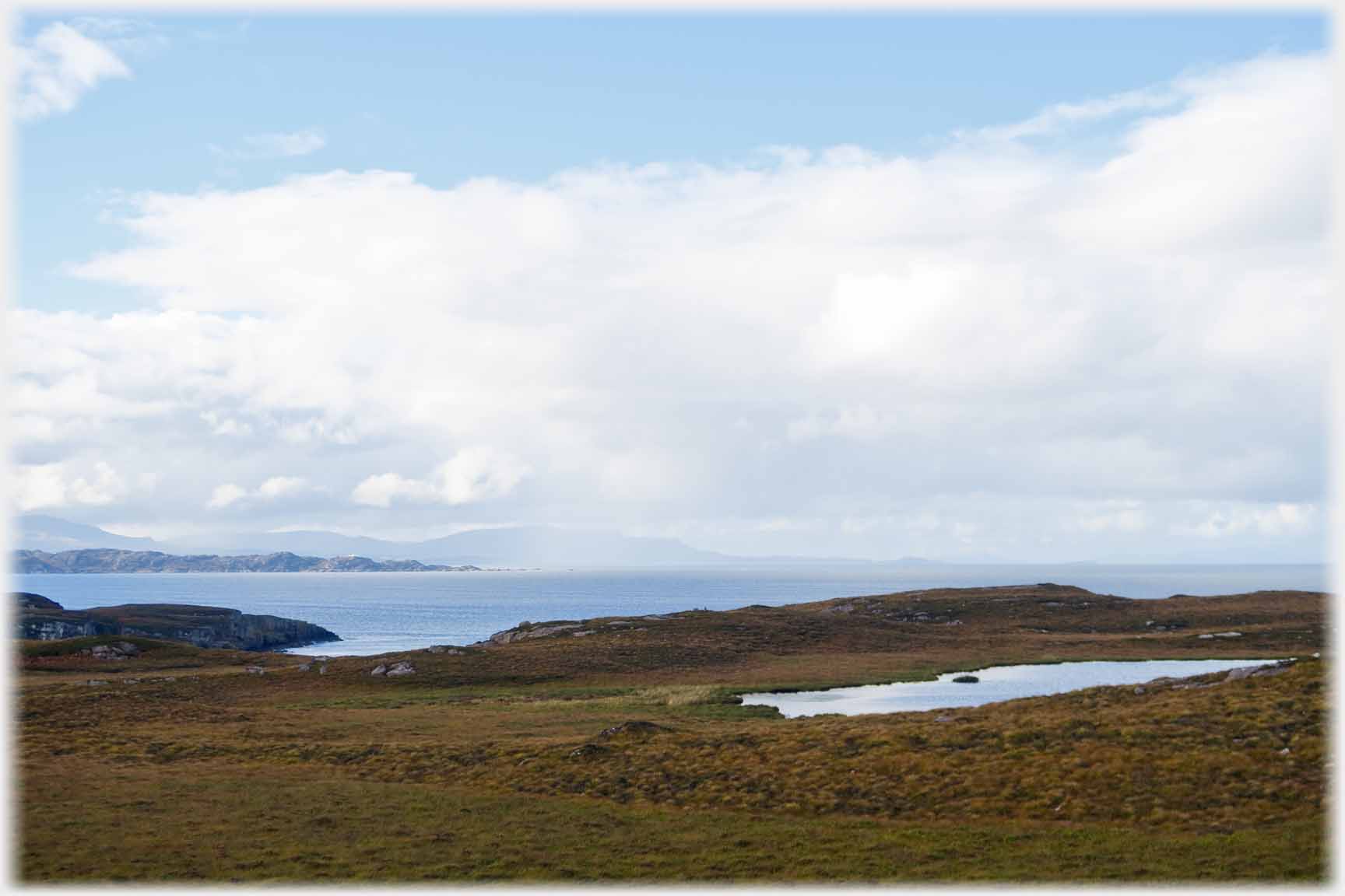 Light foregound with lochan shower over hills on horizon across the sea.