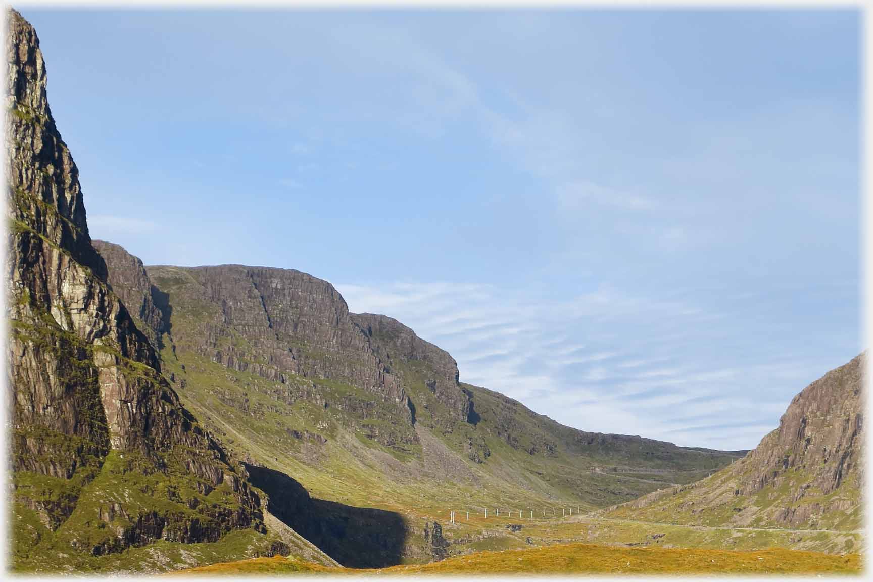 Looking up a wide valley with high butresses to the left, and just distinguishable roads.