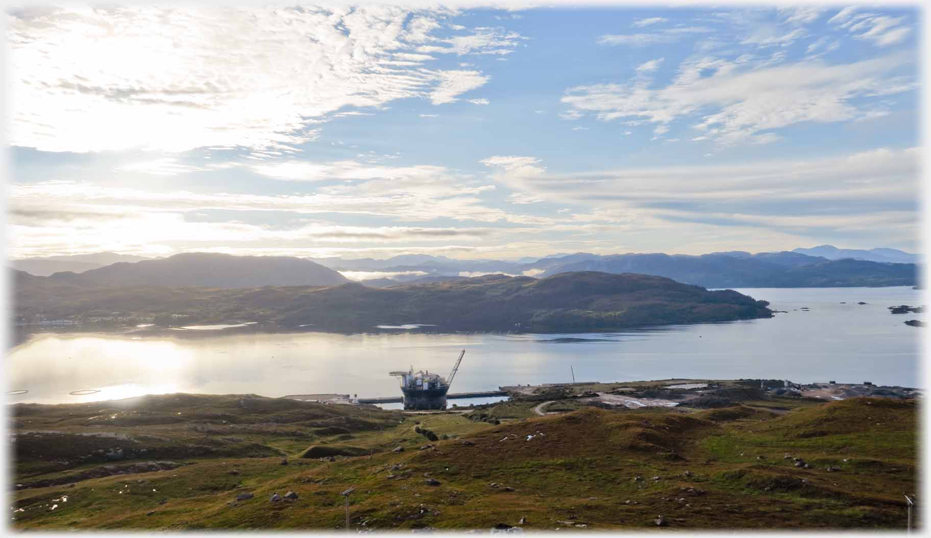 Looking down towards large ship in dock, undeveloped land around and across the water.