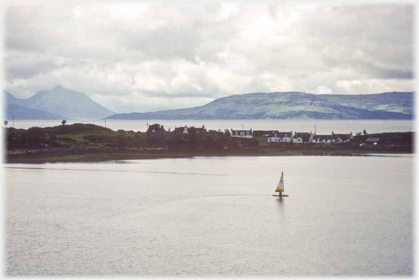 Houses on spit of land with sea in front and beyond, yacht in foreground.