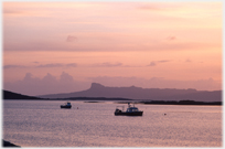 Fishing boats in sunset with islands beyond.