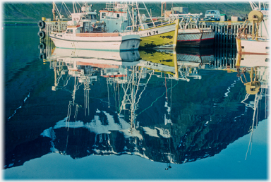 Boat reflections against black hills.