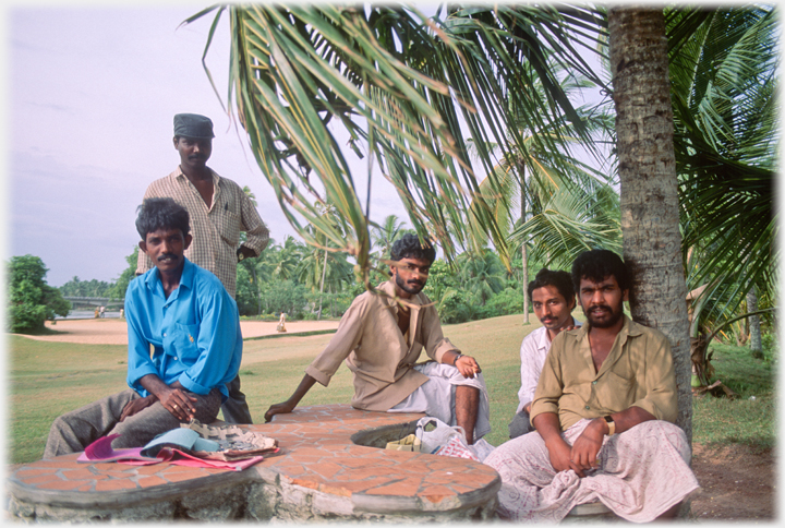 Five men by stone table under tree.