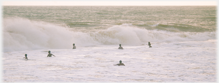 Six men in the sea waiting for an approaching wave.