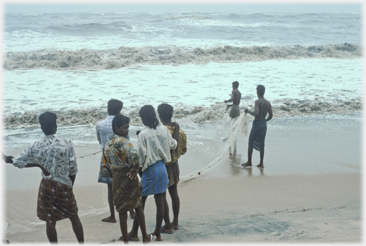 Four fishermen with their net, three students stand close by watching.