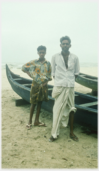 Two men standing beside boats.