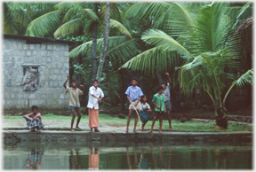 Group of children waving from river bank.