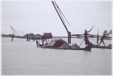 Two foreground punts and many huts on platforms beyond.