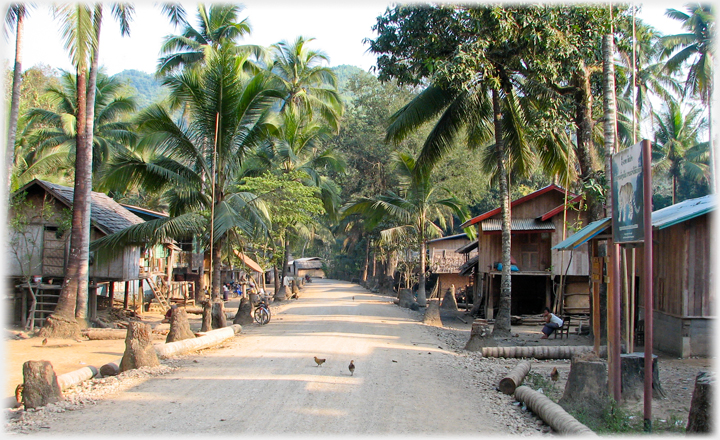 View across the width of a village street, two chickens in centre of the road.