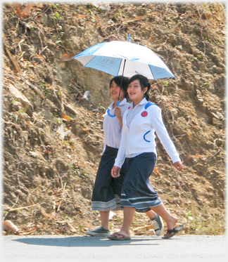 Two girls under umbrells passing.
