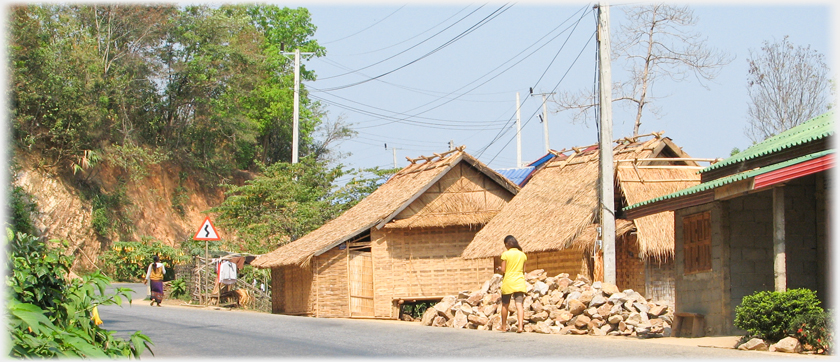 Village street with two pedestrians, houses with woven walls.