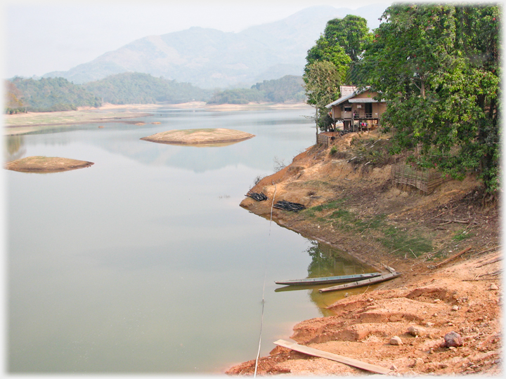 House perched on the fiver bank, hills in distance and canoes moored.