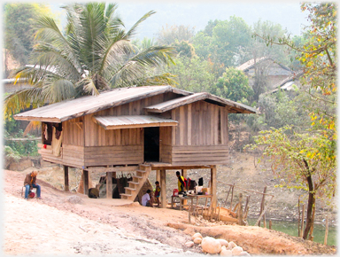 A new looking stilt house at the roadside with people near by.