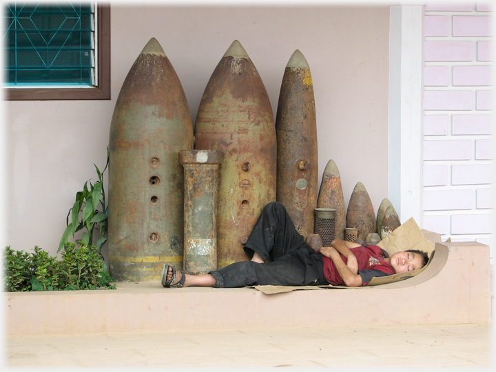 Person asleep on the ground next to bombs.