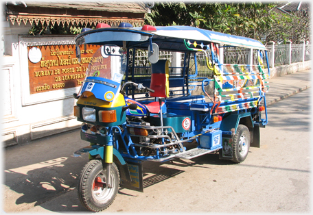 Long bodied well decorated motor-tricycle with seats for 8 people facing inwards.
