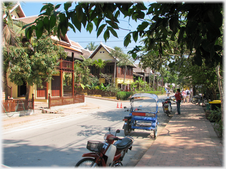 Street with large houses to left and parked motorbikes.