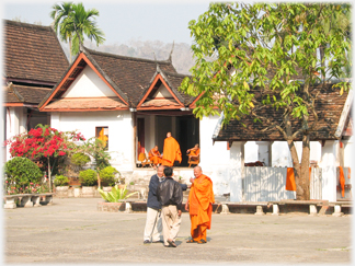 A senior monk meets with two lay people in the courtyard.