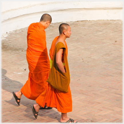 Two monks walking one with brown bag, one swathed.
