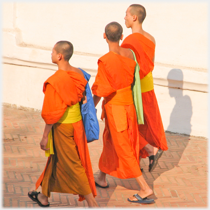 Three monks walking one with blue bag, one green bag and yellow belts.
