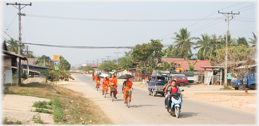 Line of monks on bicycles with motorcyclist in front.